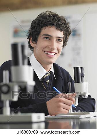 Stock Photo - High school student using microscope and taking notes in classroom. Fotosearch
