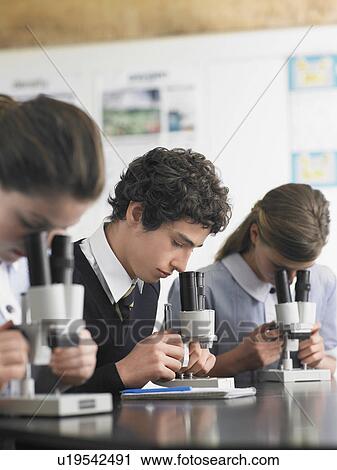 Stock Image - High school students using microscopes in classroom. Fotosearch