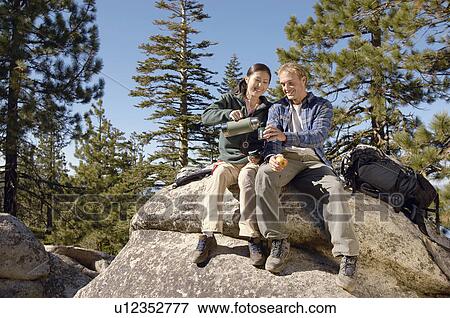 Hikers relaxing on boulder near forest View Large Photo Image Stock Photo - Hikers relaxing on boulder near forest. Fotosearch