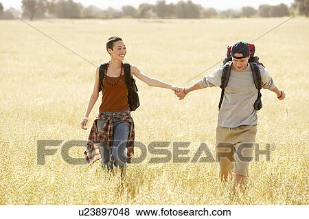 Hiking couple holding hands, walking through field View Large Photo Image Stock Photo - Hiking couple holding hands, walking through field. Fotosearch