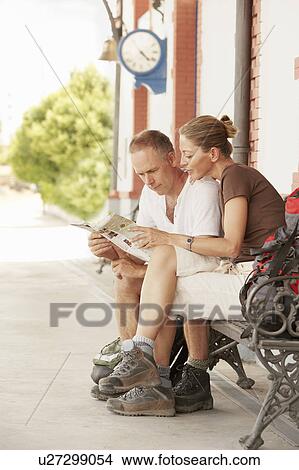 Picture - Hiking couple looking at map, sitting on railway platform. Fotosearch