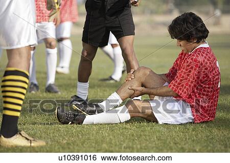 Stock Photograph - Injured soccer player sitting on pitch, portrait. Fotosearch