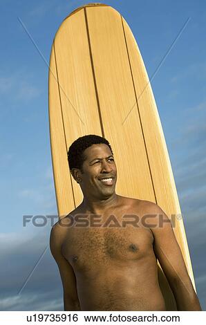Stock Photograph - Male surfer by surfboard, outdoors. Fotosearch