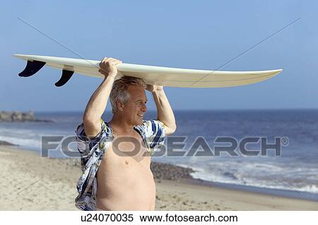 Stock Photography - Male surfer carrying surfboard on beach. Fotosearch