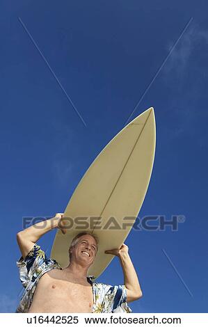 Stock Photography - Male surfer carrying surfboard on head, (low angle view). Fotosearch