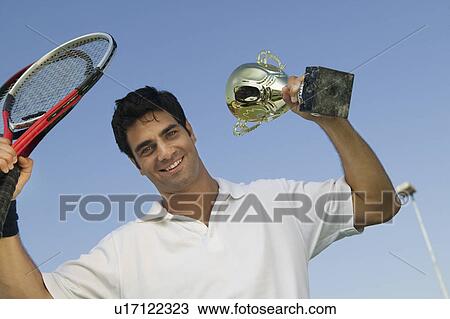 Stock Image - Male Tennis Player raising tennis rackets and Trophy, portrait. Fotosearch
