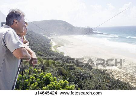 Picture - Man and Daughter Looking out at Ocean from balcony of vacation house, side view. Fotosearch