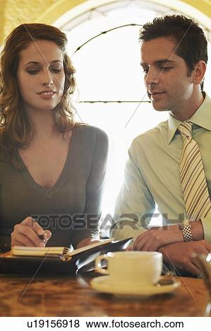 Man and woman sitting in cafe, looking at daily organizer. View Large Photo Image Stock Photo - Man and woman sitting in cafe, looking at daily organizer.. Fotosearch