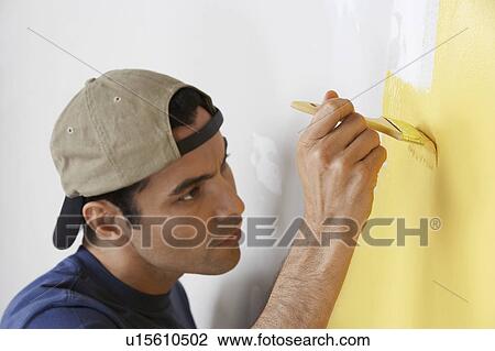 Stock Image - Man carefully painting interior wall, close-up. Fotosearch