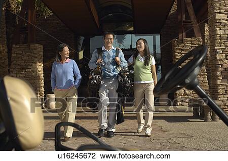 Stock Image - Man Carrying Girlfriend's Golf Clubs to Golf Cart, mother walking beside. Fotosearch