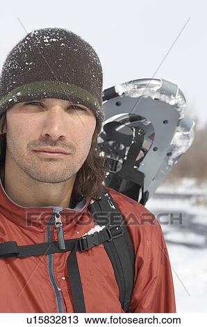 Stock Image - Man carrying snow shoes in snow, head and shoulders. Fotosearch