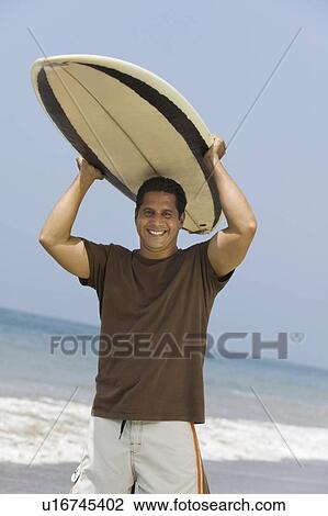 Stock Image - Man Carrying Surfboard Over His Head. Fotosearch