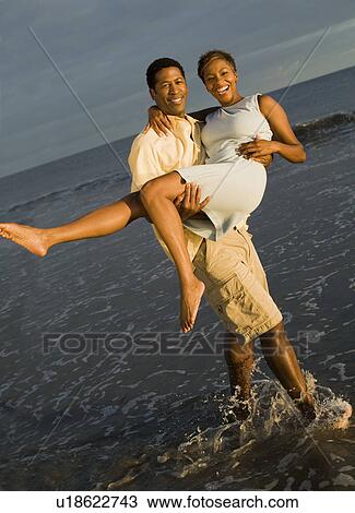 Man carrying woman at ocean, (portrait) View Large Photo Image Stock Image - Man carrying woman at ocean, (portrait). Fotosearch
