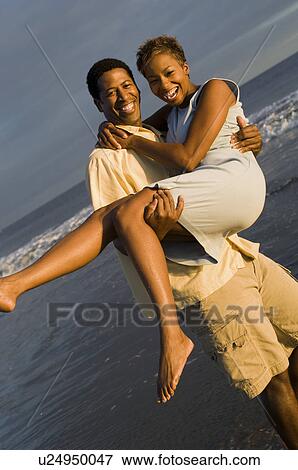 Stock Photo - Man carrying woman at ocean, (portrait). Fotosearch