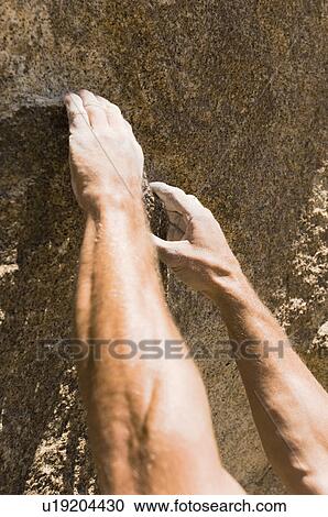 Stock Image - Man climbing on rock, close-up on hands. Fotosearch