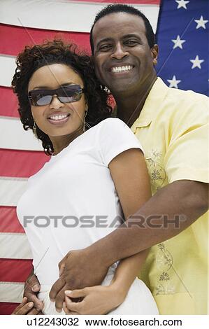 Stock Image - Man embracing woman, American flag in background, (portrait). Fotosearch