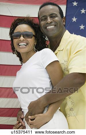 Stock Image - Man embracing woman, American flag in background, (portrait). Fotosearch