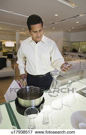 Stock Photo - Man Examining Kitchenware in furniture store. Fotosearch