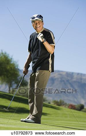 Stock Image - Man gesturing on golf course, smiling, (portrait). Fotosearch