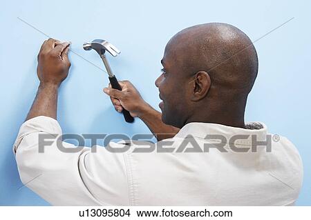 Picture - Man hammering nail into wall, back view. Fotosearch
