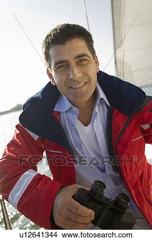 Man holding binoculars on yacht, (portrait) View Large Photo Image Picture - Man holding binoculars on yacht, (portrait). Fotosearch