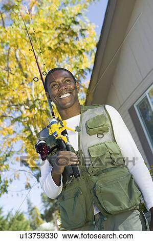 Man holding fishing rod in font of house, smiling, (low angle view) View Large Photo Image Stock Image - Man holding fishing rod in font of house, smiling, (low angle view). Fotosearch