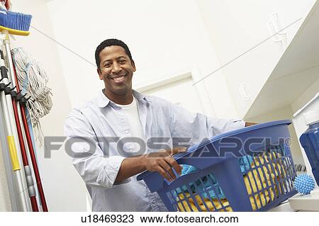 Stock Image - Man holding laundry basket, portrait. Fotosearch