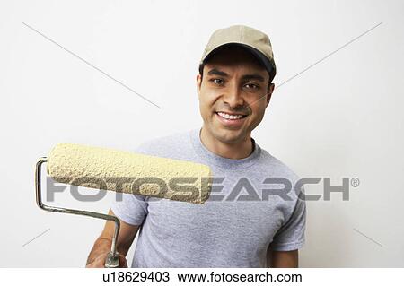 Stock Image - Man holding paint roller, portrait. Fotosearch