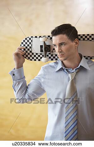 Picture - Man holding skateboard behind head, portrait. Fotosearch