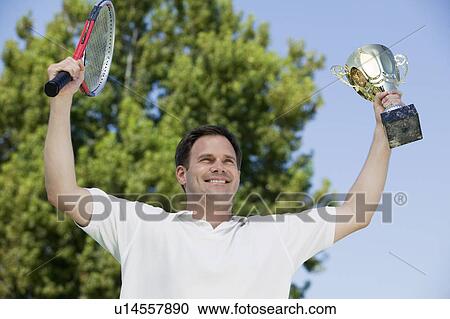Man Holding up Tennis Rackets and Trophy on tennis court, low angle view View Large Photo Image Stock Image - Man Holding up Tennis Rackets and Trophy on tennis court, low angle view. Fotosearch