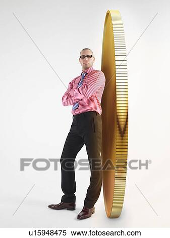 Stock Photography - Man in glasses leaning against giant coin, digital composite. Fotosearch