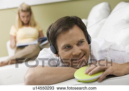 Stock Image - Man Listening to Music While Wife Reads. Fotosearch