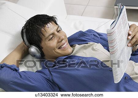 Man lying on sofa Listening to Music and Reading Magazine, high angle view View Large Photo Image Picture - Man lying on sofa Listening to Music and Reading Magazine, high angle view. Fotosearch