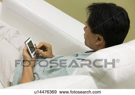 Stock Photo - Man on Couch Using PDA, high angle view. Fotosearch