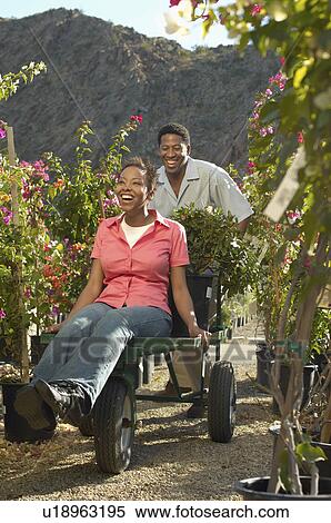 Man pushing woman on cart at plant nursery View Large Photo Image Stock Photography - Man pushing woman on cart at plant nursery. Fotosearch