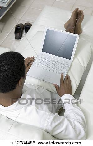 Man reclining on sofa using laptop, high angle view View Large Photo Image Stock Photograph - Man reclining on sofa using laptop, high angle view. Fotosearch