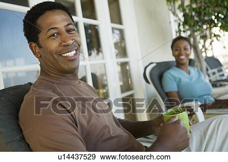 Man relaxing on porch, wife in background, (portrait) View Large Photo Image Stock Photo - Man relaxing on porch, wife in background, (portrait). Fotosearch