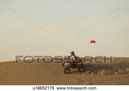 Stock Photo - Man riding quad bike on sand. Fotosearch