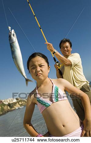 Picture - Man showing fish to daughter (7-9) at ocean. Fotosearch