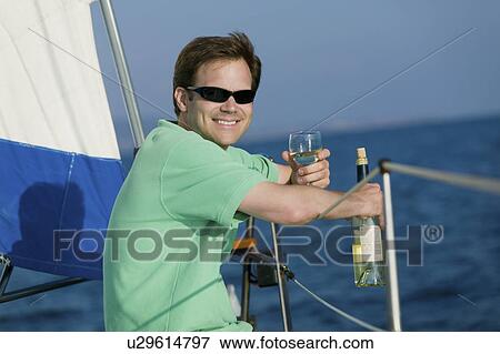Man sitting on sailboat, drinking white wine, (portrait) View Large Photo Image Stock Photo - Man sitting on sailboat, drinking white wine, (portrait). Fotosearch