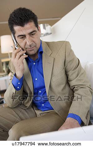 Man sitting on sofa in Furniture Store talking on cell phone View Large Photo Image Picture - Man sitting on sofa in Furniture Store talking on cell phone. Fotosearch