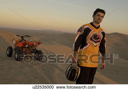 Man standing by quad bike in desert at sunset View Large Photo Image Stock Image - Man standing by quad bike in desert at sunset. Fotosearch