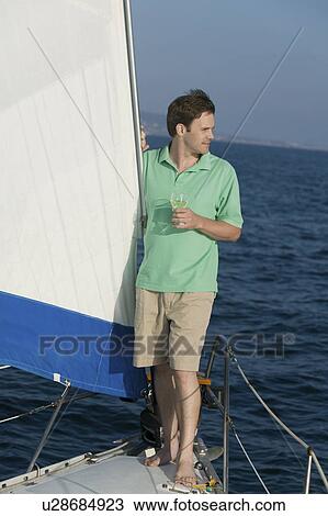 Man standing on sailboat, holding glass of white wine View Large Photo Image Stock Image - Man standing on sailboat, holding glass of white wine. Fotosearch