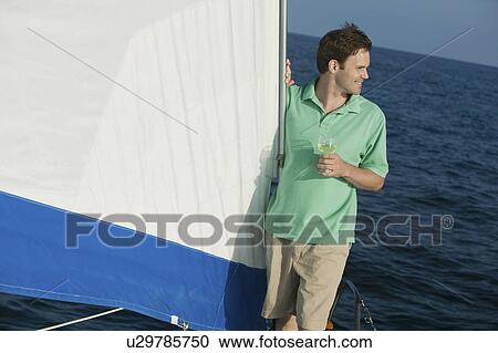 Stock Image - Man standing on sailboat, holding glass of white wine. Fotosearch