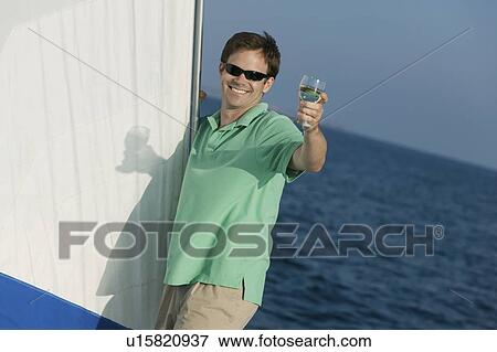 Man standing on sailboat, toasting with glass of white wine, (portrait) View Large Photo Image Stock Photo - Man standing on sailboat, toasting with glass of white wine, (portrait). Fotosearch