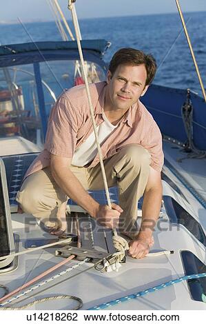 Man standing on sailboat tying rope, (portrait) View Large Photo Image Stock Image - Man standing on sailboat tying rope, (portrait). Fotosearch
