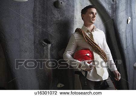 Stock Image - Man standing with climbing equipment at base of wall, portrait. Fotosearch
