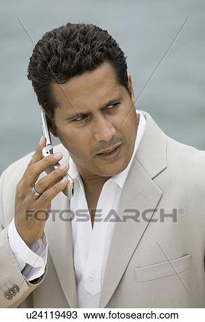 Stock Image - Man talking on mobile phone by water. Fotosearch