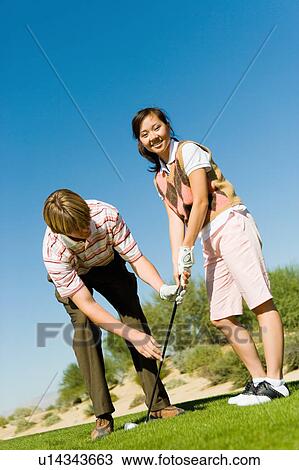 Stock Image - Man teaching teenage girl to putt. Fotosearch