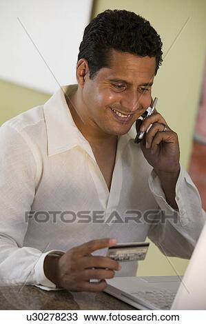Man Using Cell Phone and laptop to purchase with credit card at home View Large Photo Image Stock Image - Man Using Cell Phone and laptop to purchase with credit card at home. Fotosearch